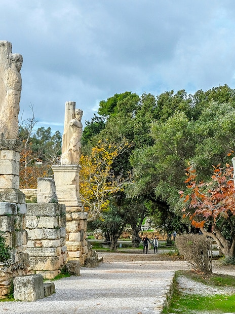 Odeon of Agrippa statues in Ancient Agora, Athens, with trees and ruins in the background.