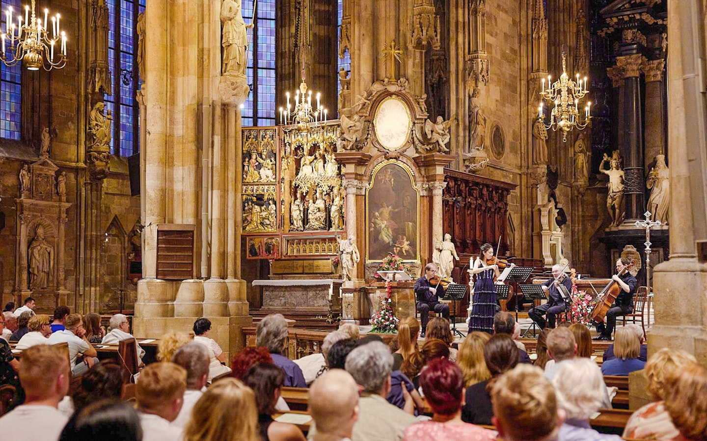 Orchestra performing inside St. Stephen's Cathedral, Vienna, with audience seated in pews.
