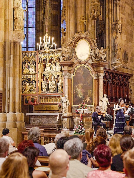Orchestra performing inside St. Stephen's Cathedral, Vienna, with audience seated in pews.