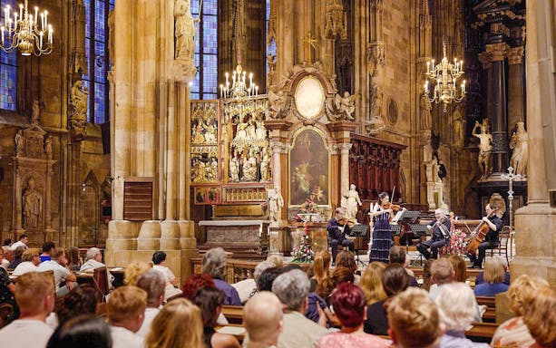 Orchestra performing inside St. Stephen's Cathedral, Vienna, with audience seated in pews.