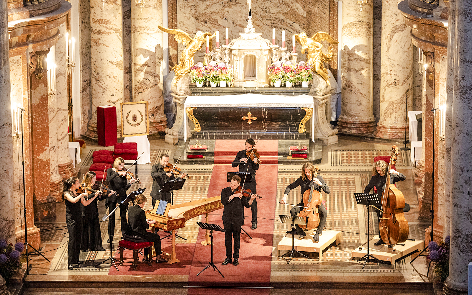 Musicians performing Vivaldi's Four Seasons inside a grand concert hall with ornate decor.