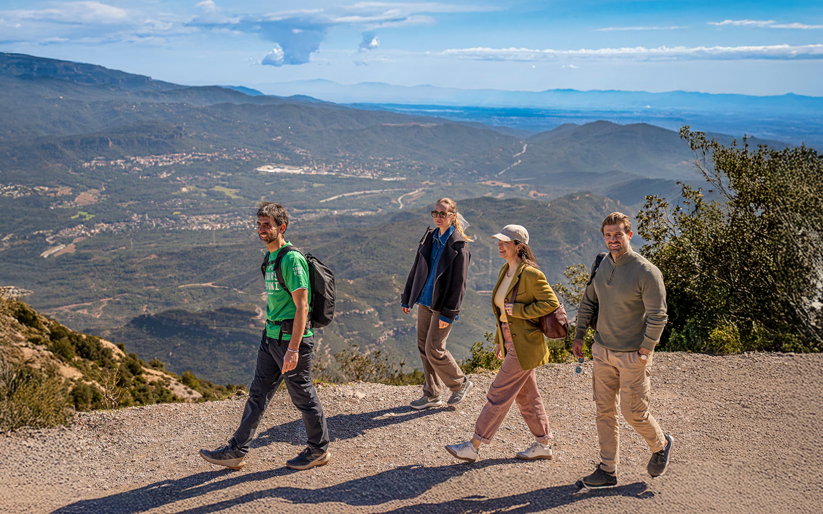 Tourists hiking with guide on Montserrat mountain trail with scenic views.