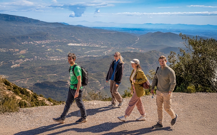 Tourists hiking with guide on Montserrat mountain trail with scenic views.
