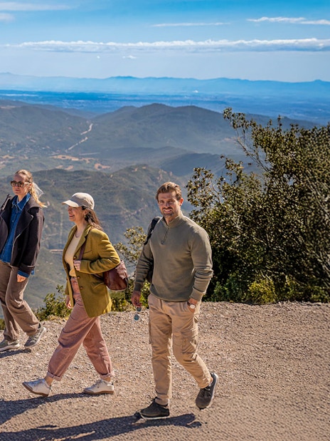 Tourists hiking with guide on Montserrat mountain trail with scenic views.