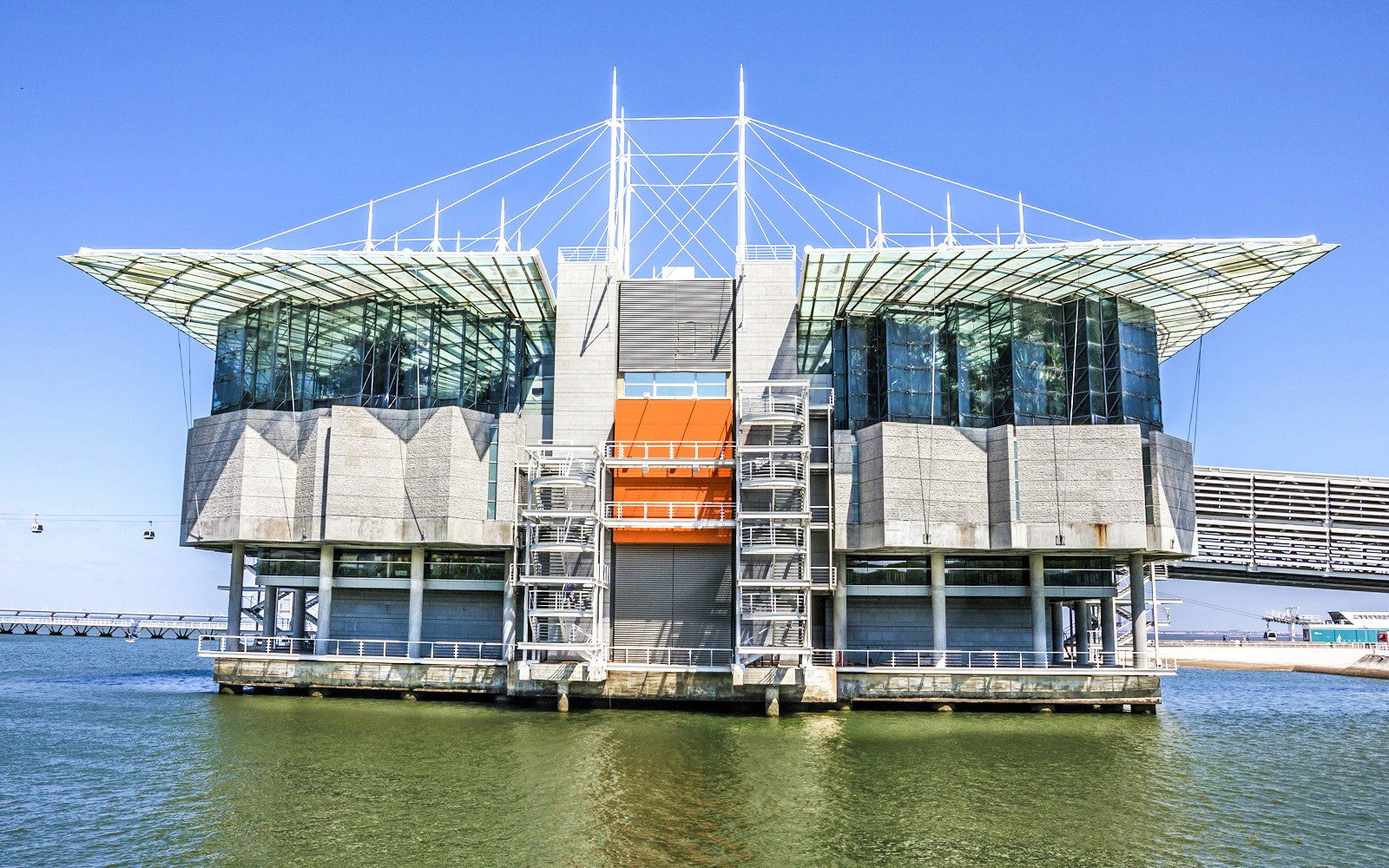 Lisbon Oceanarium exterior with water and cable cars in the background.
