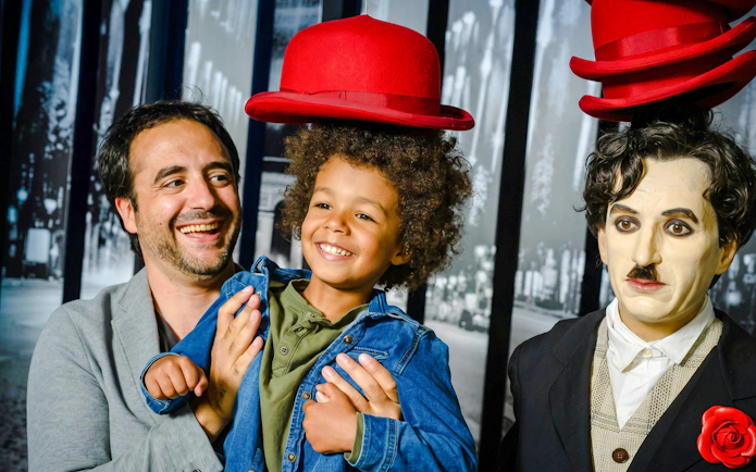 Man and child smiling next to a wax figure at Grévin Wax Museum, Paris.