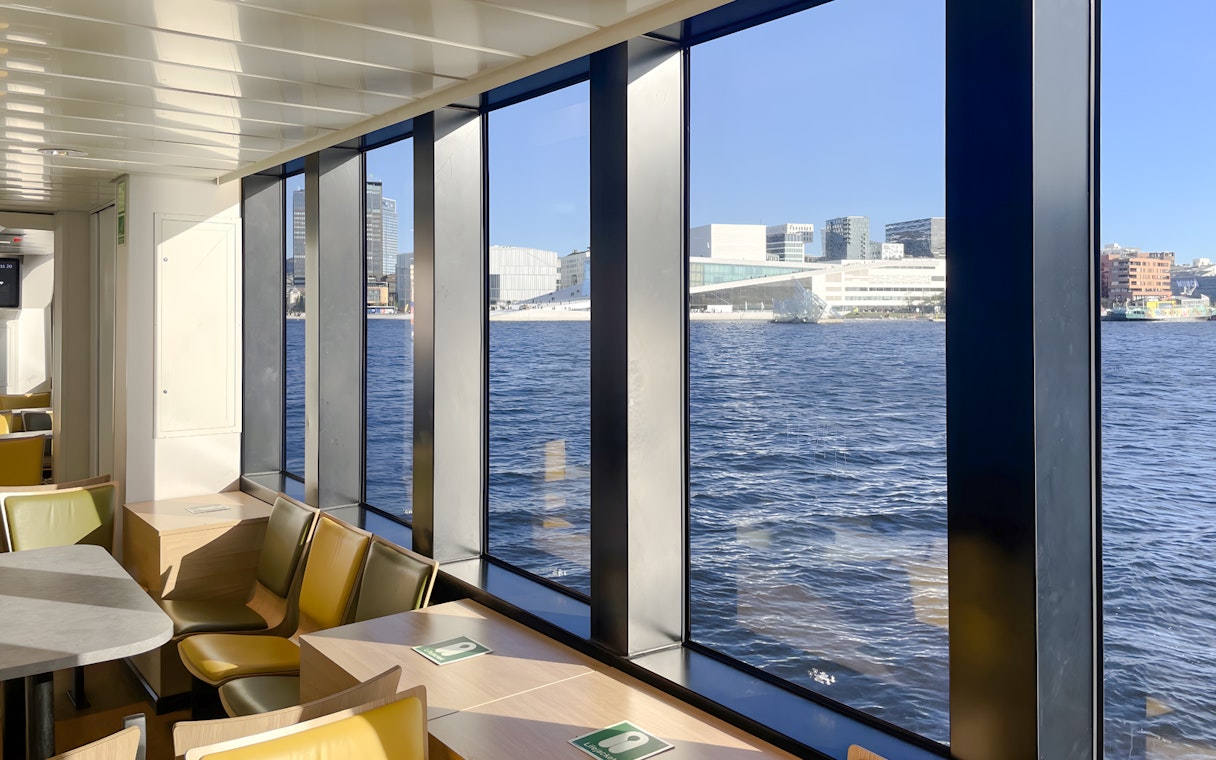 Interior view of a cruise ship with large windows overlooking Oslo Fjord and cityscape.