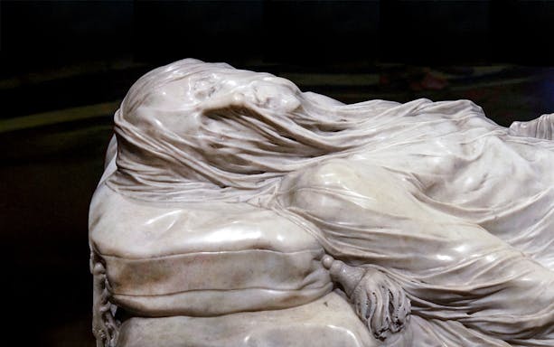 Close-up of the Veiled Christ statue in Naples, Italy, showcasing intricate marble drapery.