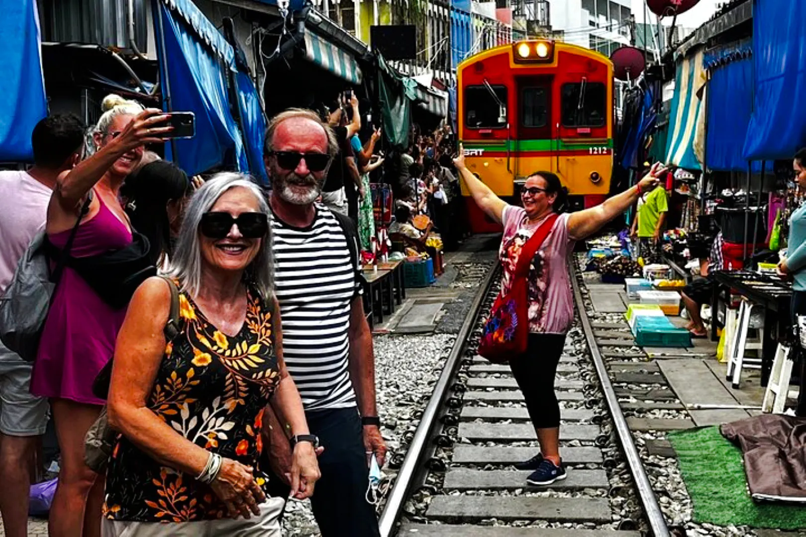 Tourists at Maeklong Railway Market with train approaching, part of Floating Market & Railway Market tour from Laem Chabang.