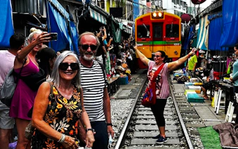 Tourists at Maeklong Railway Market with train approaching, part of Floating Market & Railway Market tour from Laem Chabang.