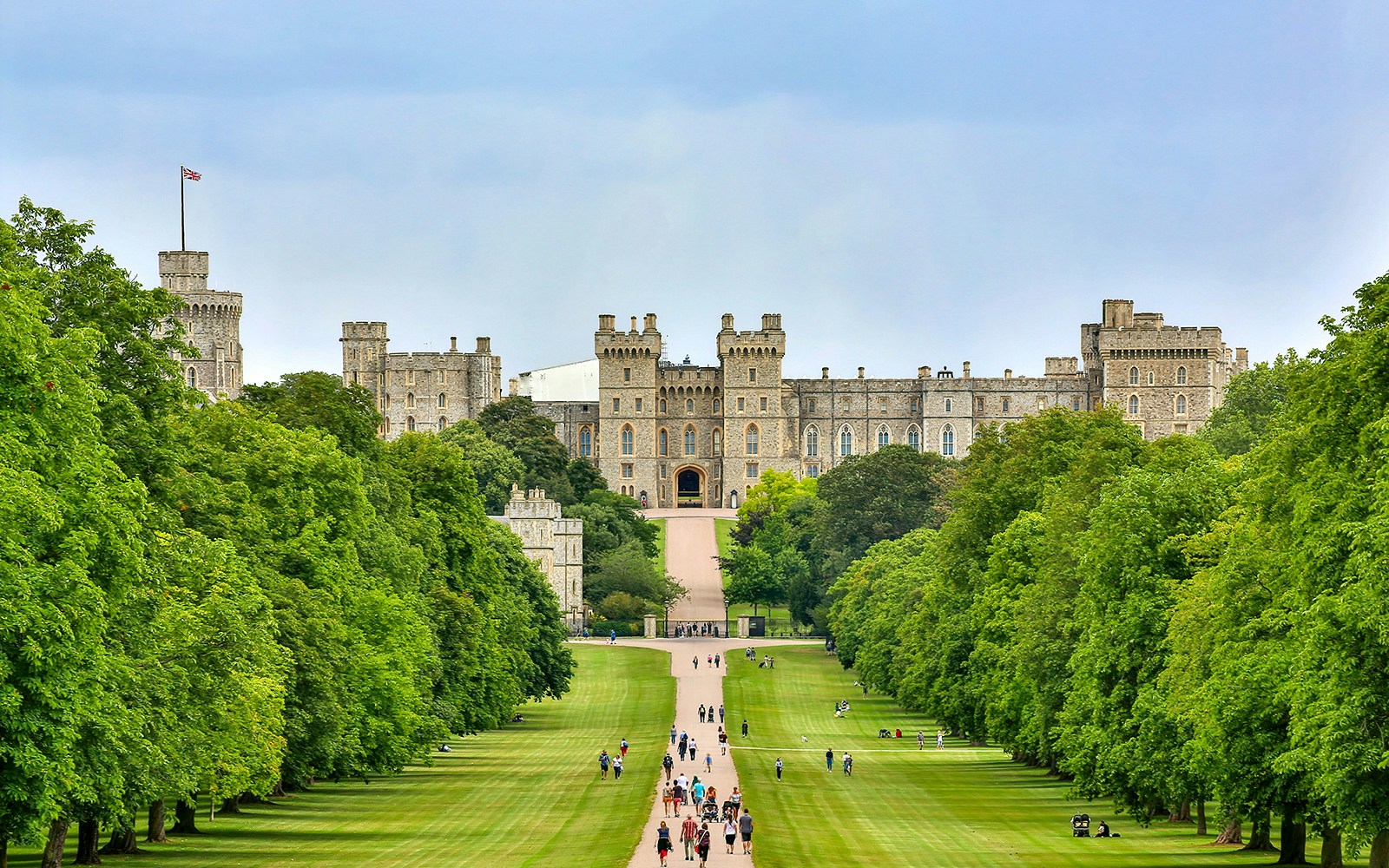 Tourists walking towards Windsor Castle through a tree-lined path on a day trip from London.