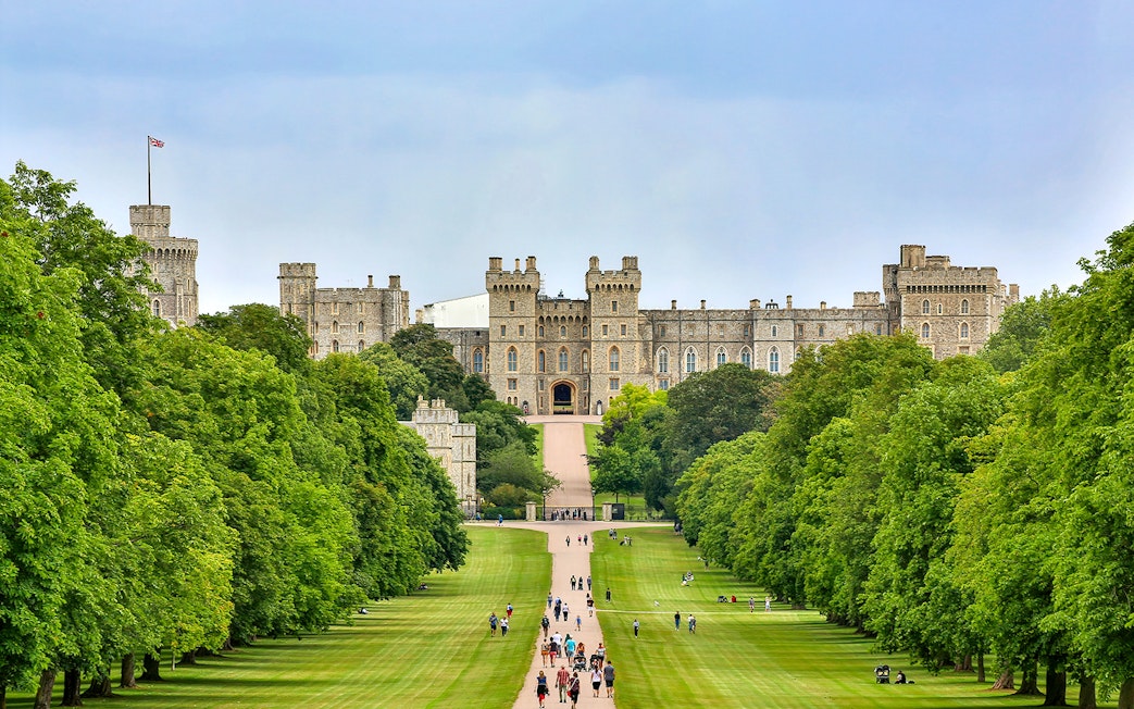 Tourists walking towards Windsor Castle through a tree-lined path on a day trip from London.