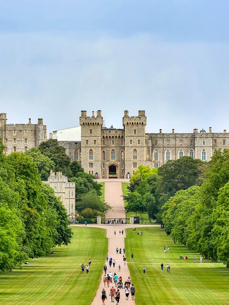 Tourists walking towards Windsor Castle through a tree-lined path on a day trip from London.