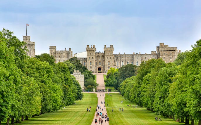 Tourists walking towards Windsor Castle through a tree-lined path on a day trip from London.