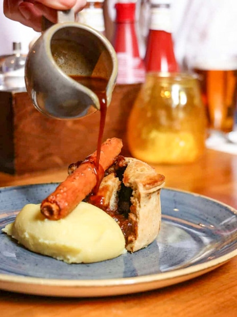 Pouring gravy over pie and mash with a pint of beer on the Eating London food tour.