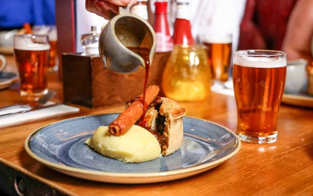 Pouring gravy over pie and mash with a pint of beer on the Eating London food tour.