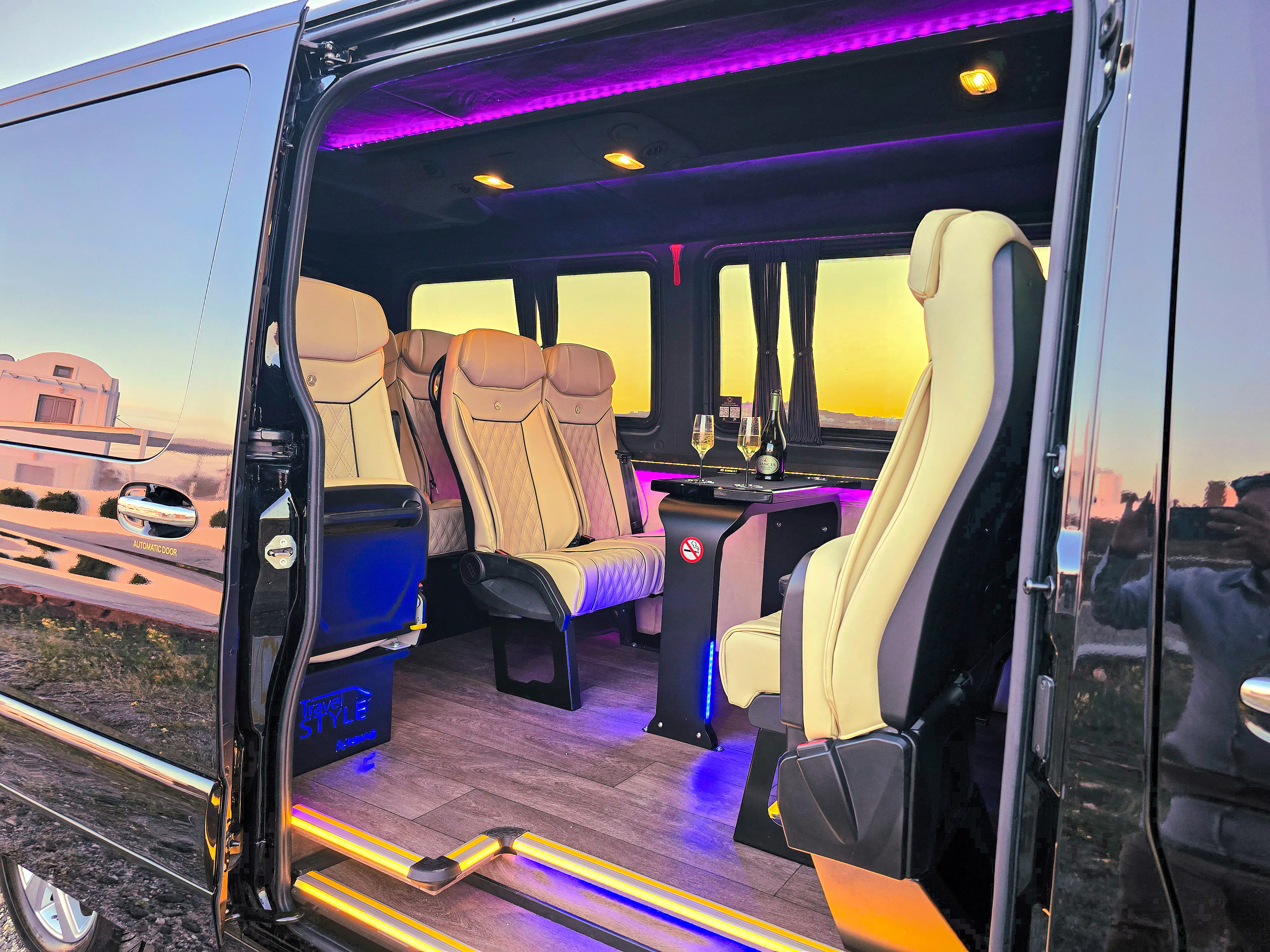 Luxury van interior for private transfer in Santorini with champagne glasses on table.