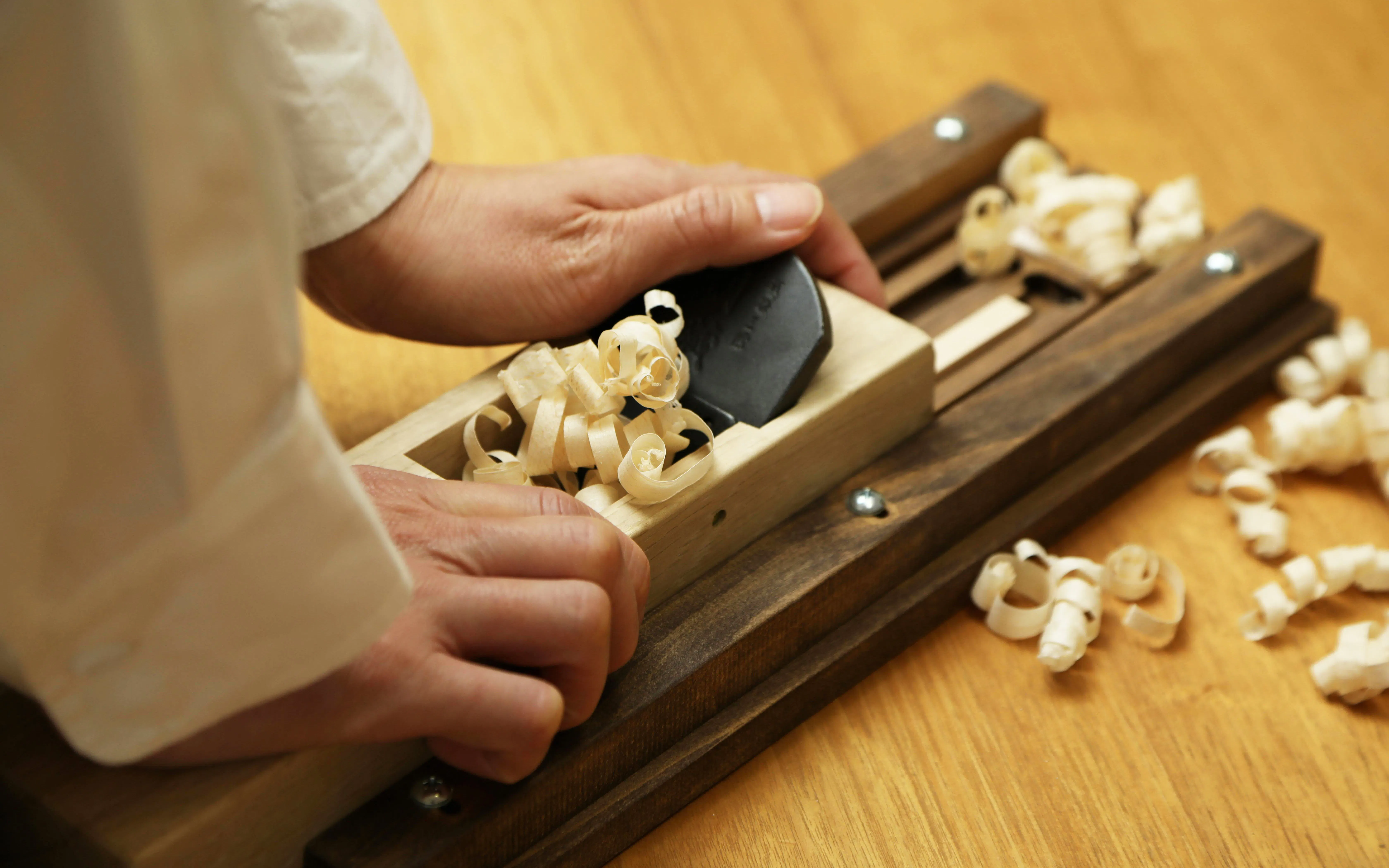 Hands crafting chopsticks with a plane tool during a workshop in Ginza.