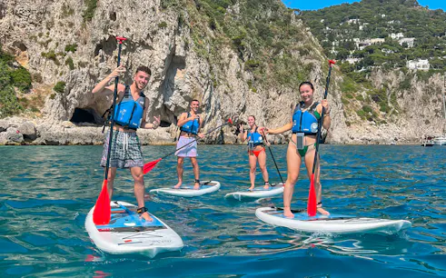 Group paddleboarding near rocky cliffs in Capri.