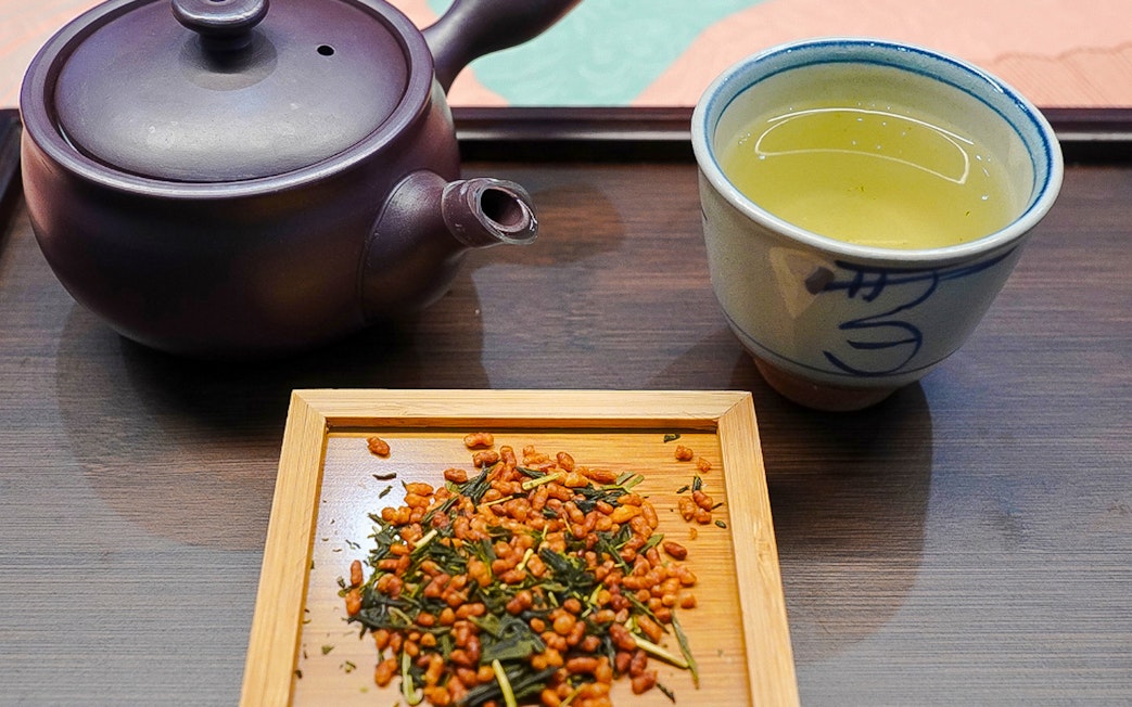 Japanese tea set with teapot, cup of green tea, and roasted rice tea leaves on a tray.
