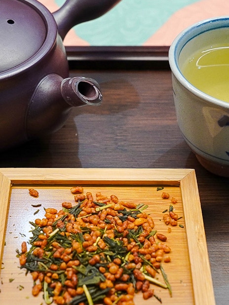 Japanese tea set with teapot, cup of green tea, and roasted rice tea leaves on a tray.