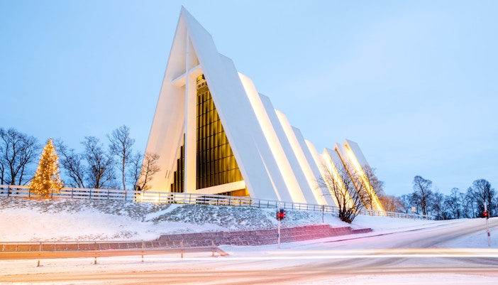 Arctic Cathedral in Tromsø illuminated at dusk with snow-covered surroundings.