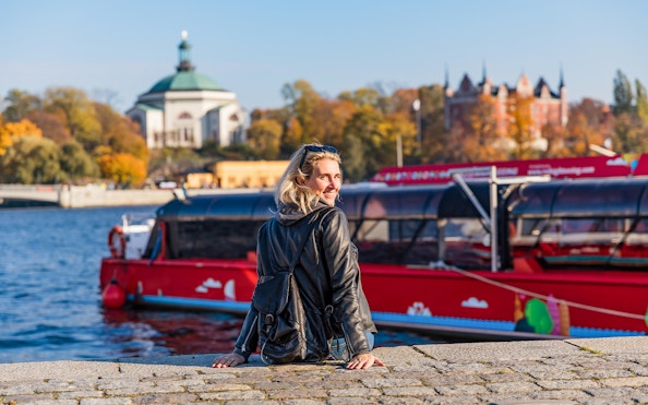 Woman at dock with red boat, ready for Stockholm tour.
