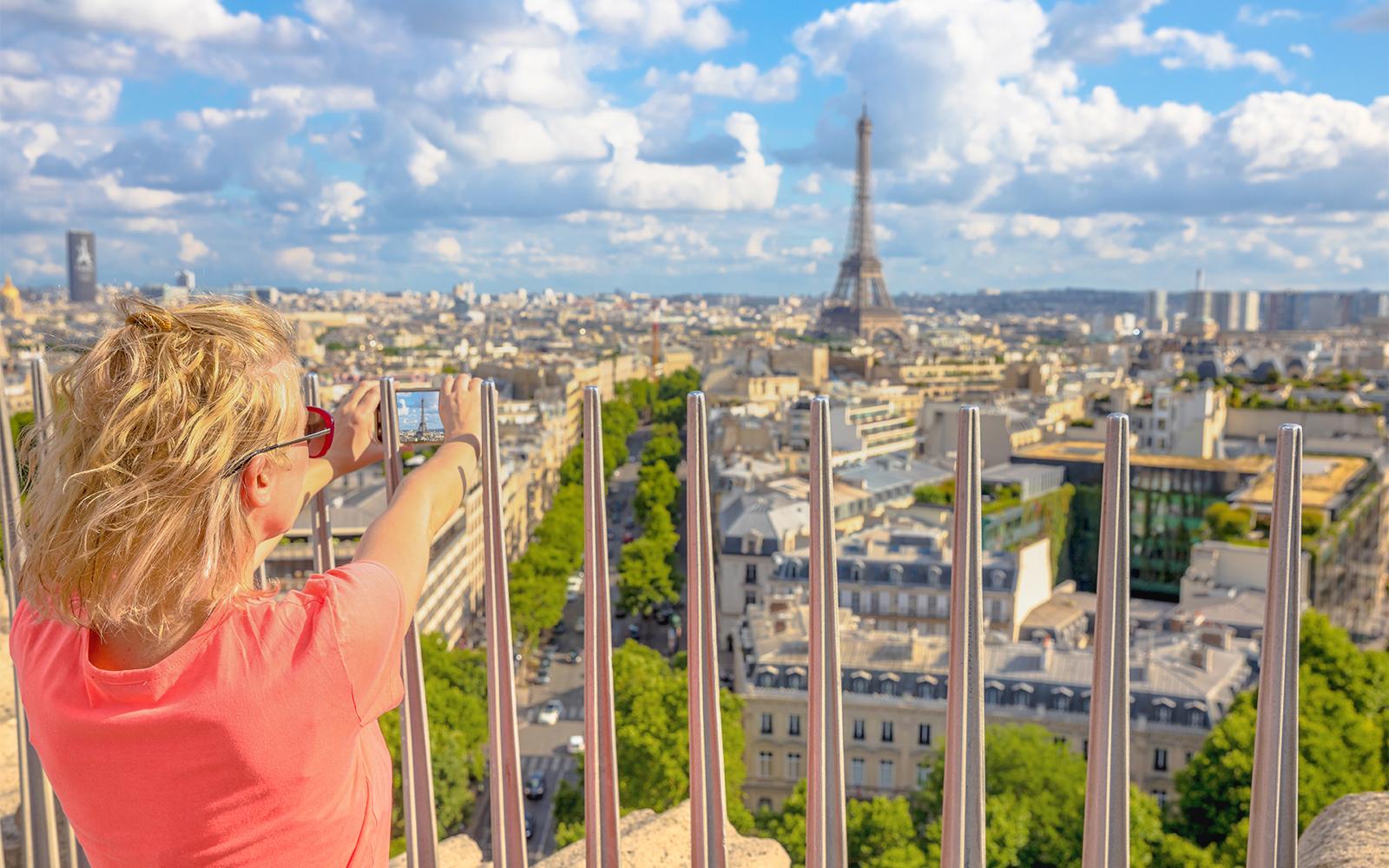 Person photographing Paris skyline with Eiffel Tower from Arc de Triomphe viewpoint.