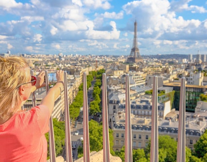 Person photographing Paris skyline with Eiffel Tower from Arc de Triomphe viewpoint.