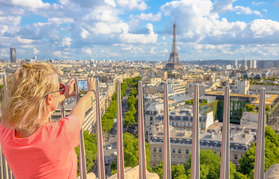 Person photographing Paris skyline with Eiffel Tower from Arc de Triomphe viewpoint.