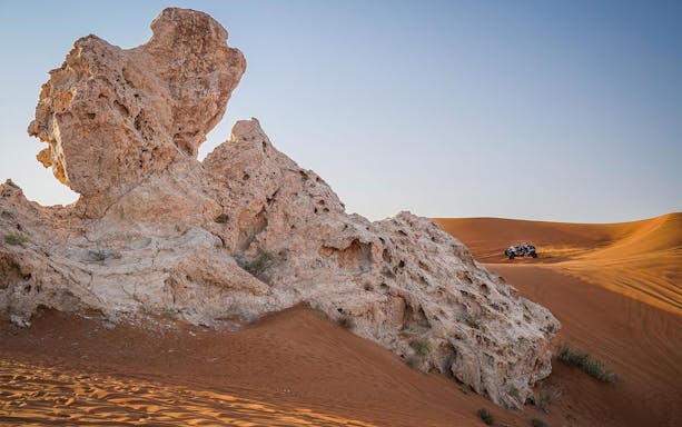 Dune buggy driving across sandy landscape near rock formations in Mleiha.