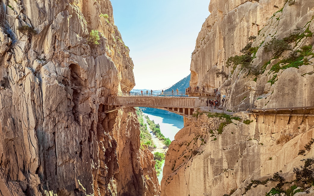 Hikers crossing a narrow bridge in Caminito del Rey, Spain, with cliffs and river below.