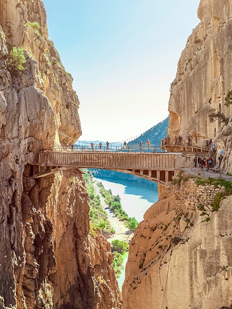 Hikers crossing a narrow bridge in Caminito del Rey, Spain, with cliffs and river below.