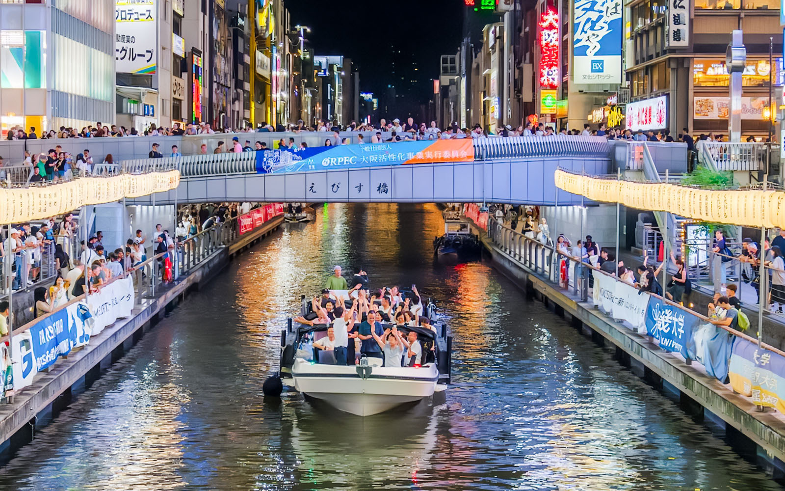 Osaka Dotonbori River Cruise boat with passengers under illuminated bridge at night.