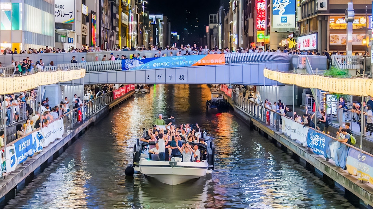 Osaka Dotonbori River Cruise boat with passengers under illuminated bridge at night.