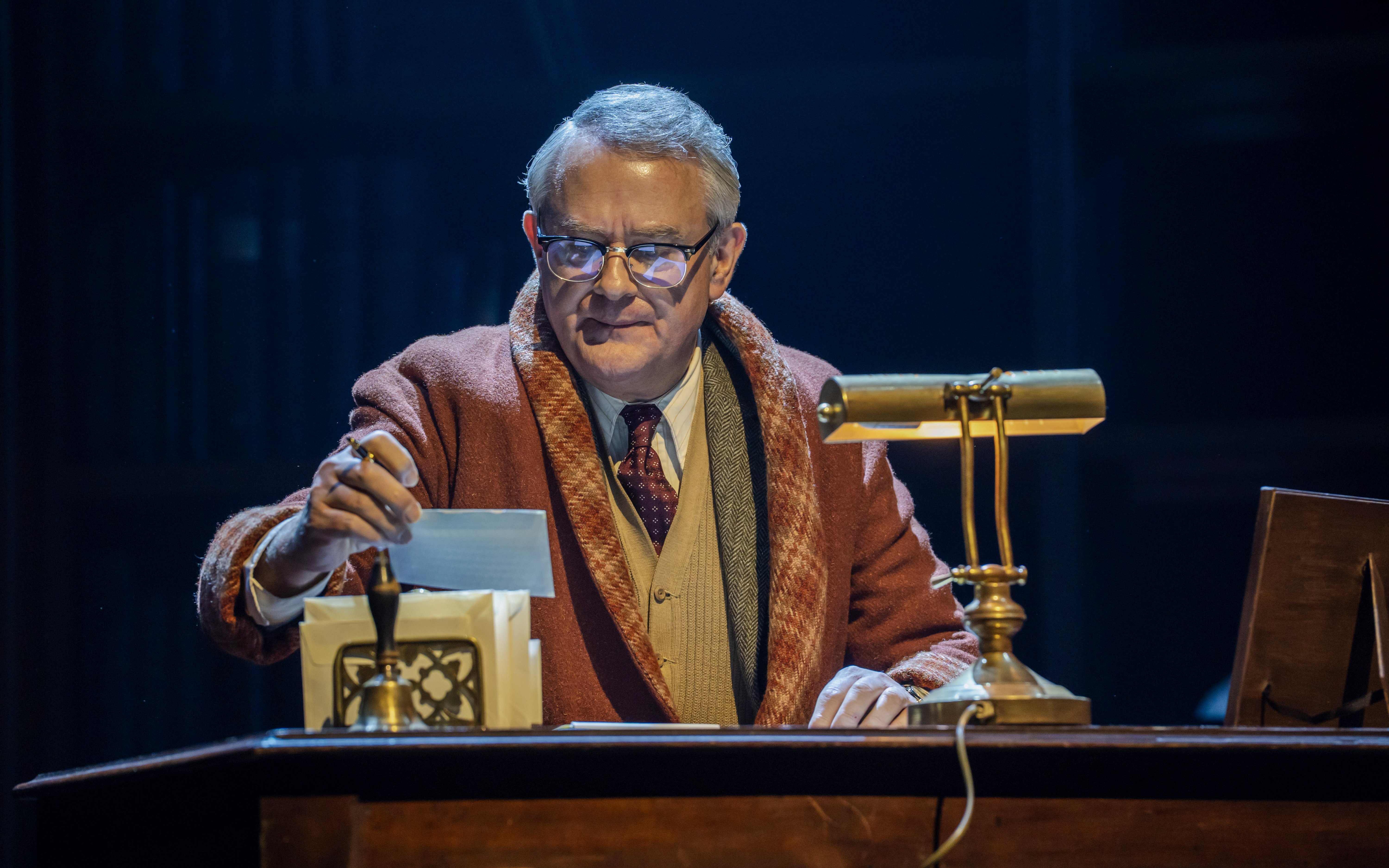 Stage scene from Shadowlands in Westend, actor at desk with lamp and papers.