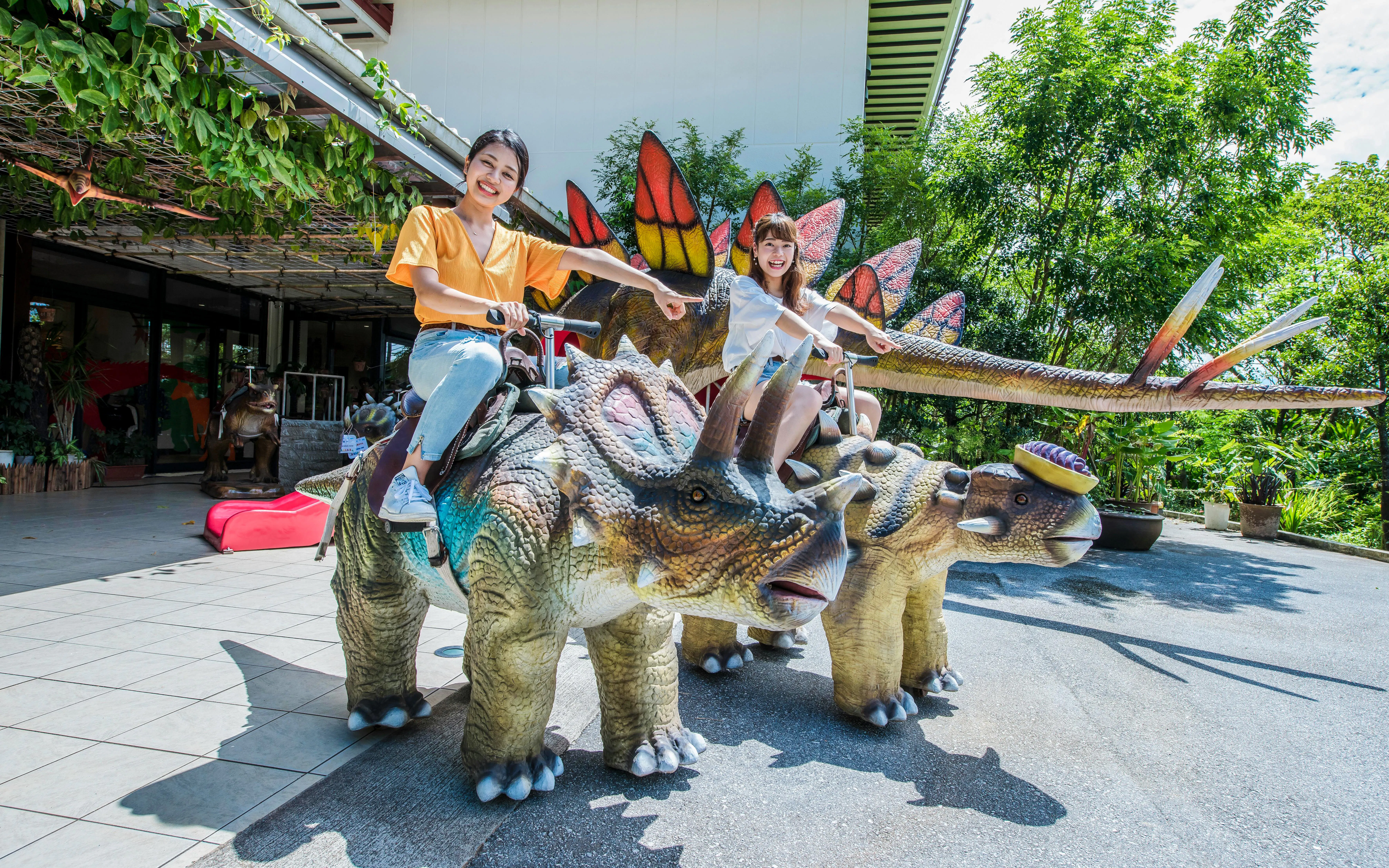 Children riding dinosaur statues at Okashigoten Nago Dino Park Yanbaru Subtropical Forest.