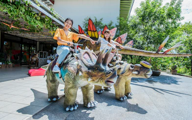 Children riding dinosaur statues at Okashigoten Nago Dino Park Yanbaru Subtropical Forest.