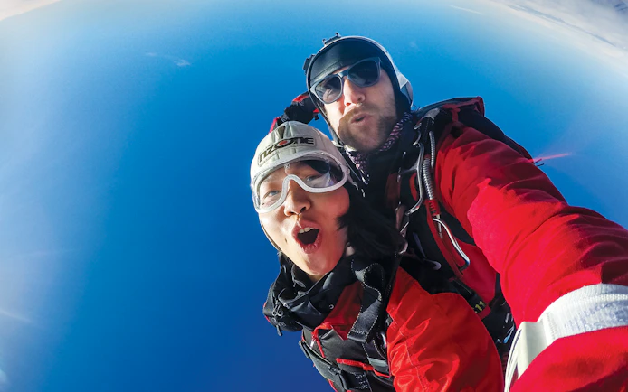 Tandem skydivers freefalling over Queenstown with clear blue sky.