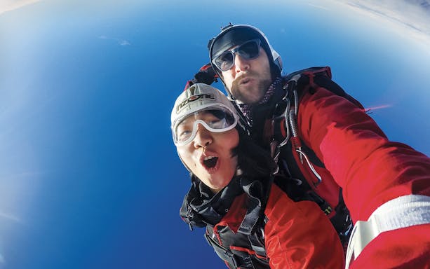 Tandem skydivers freefalling over Queenstown with clear blue sky.