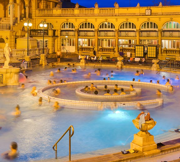 People enjoying the thermal pools at Lukacs Bath, Budapest, with historic architecture in the background.