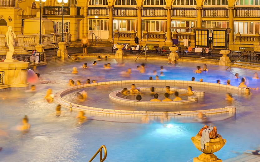 People enjoying the thermal pools at Lukacs Bath, Budapest, with historic architecture in the background.