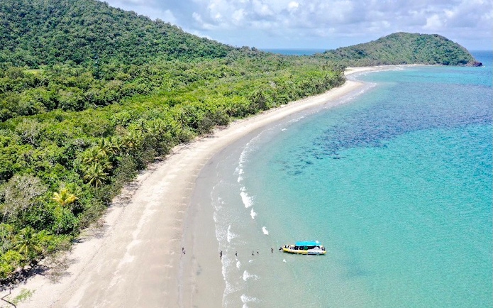 Great Barrier Reef tour boat on sandy beach with lush greenery and clear blue water.