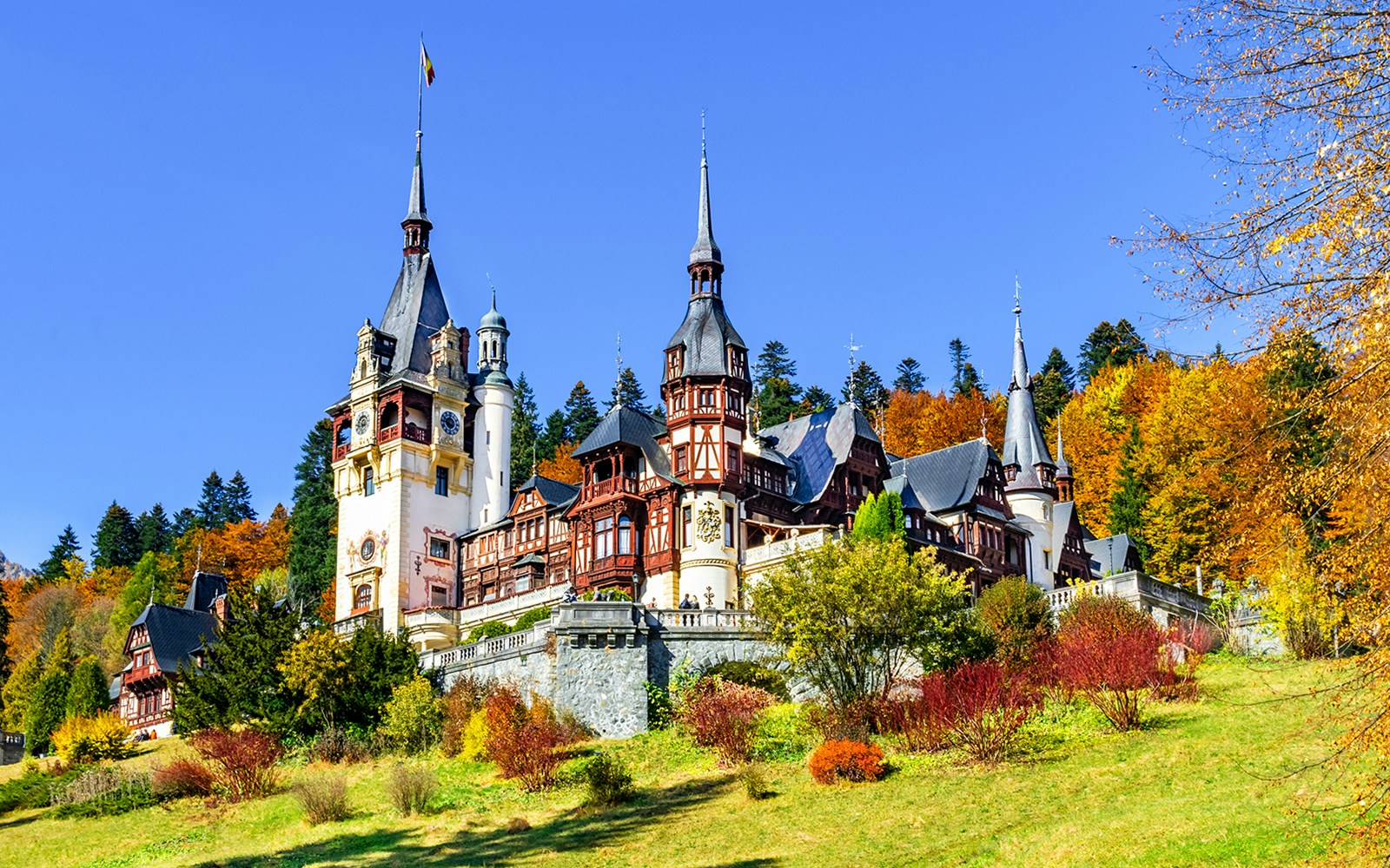 Peles Castle in Sinaia, Romania, surrounded by autumn foliage.