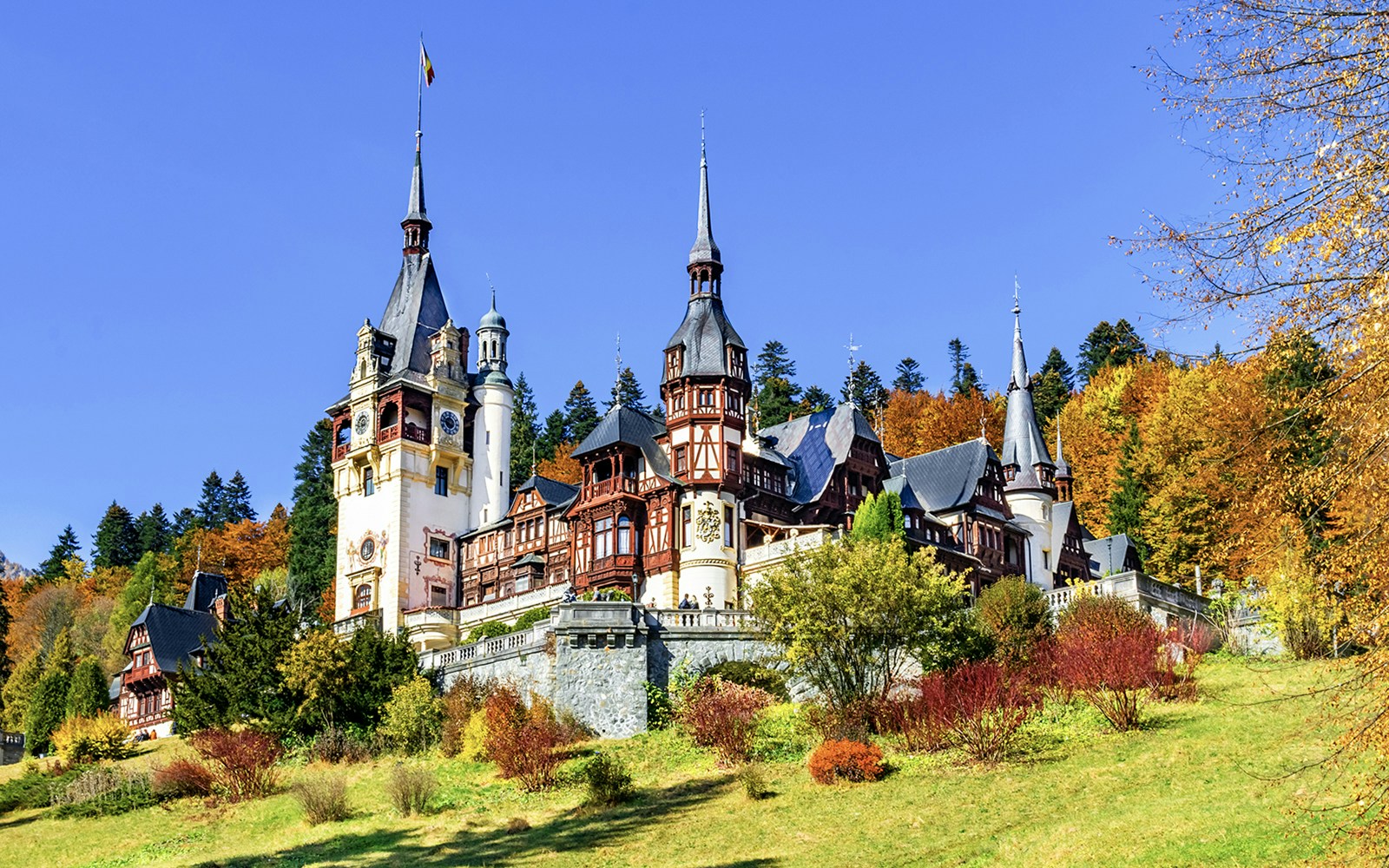 Peles Castle in Sinaia, Romania, surrounded by autumn foliage.