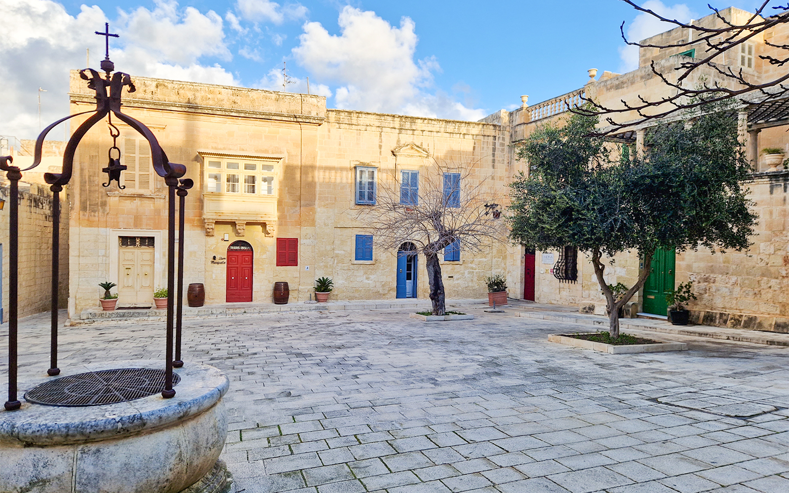 Historic courtyard in Mdina with colorful doors and a central tree.