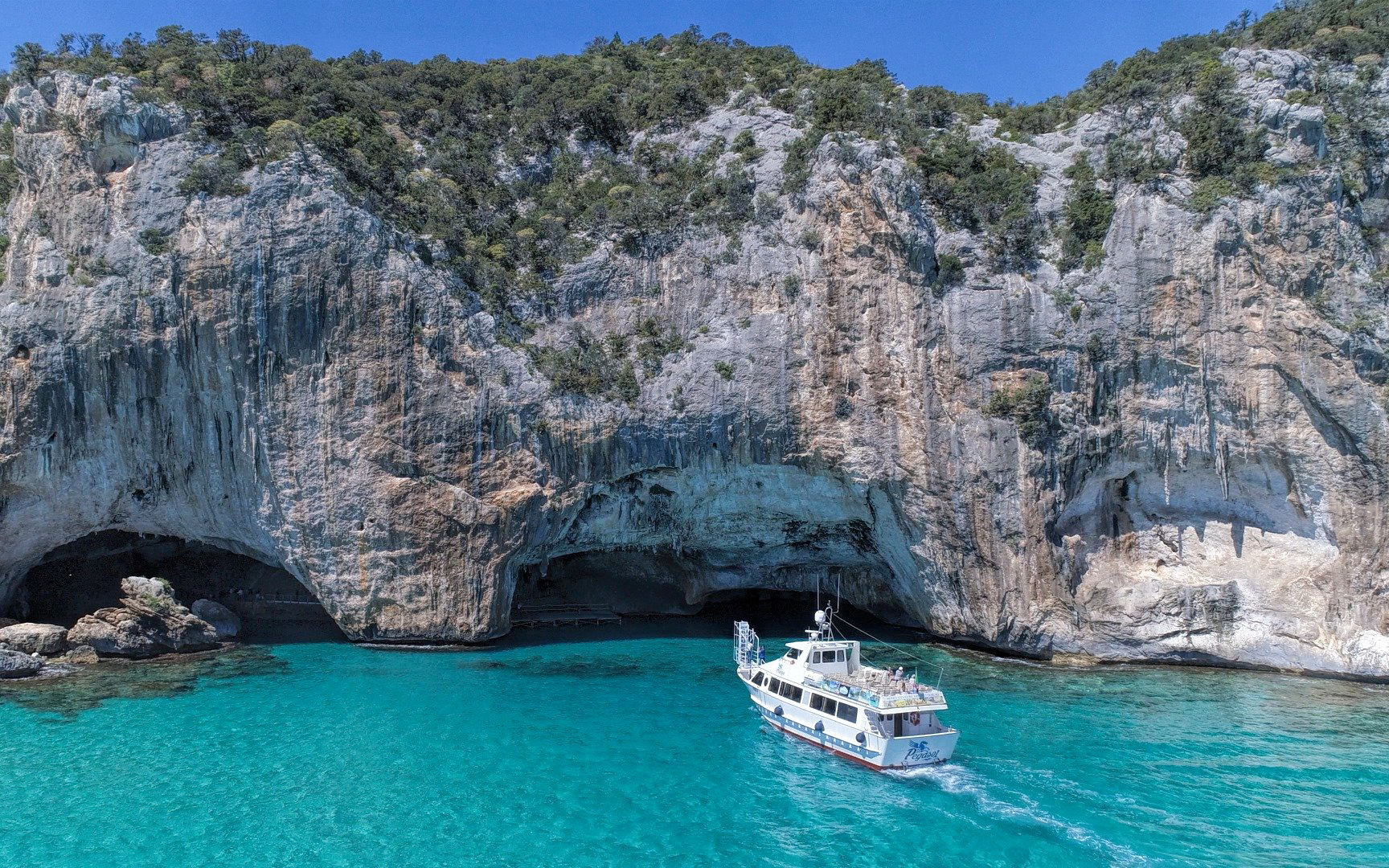Boat approaching rocky cliffs at Gulf of Orosei, Italy.