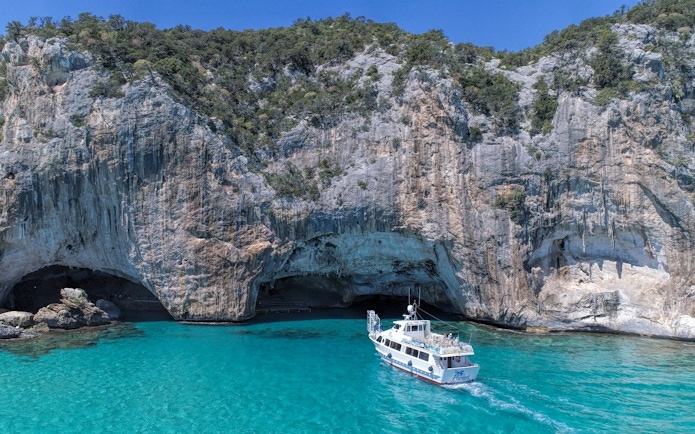 Boat approaching rocky cliffs at Gulf of Orosei, Italy.