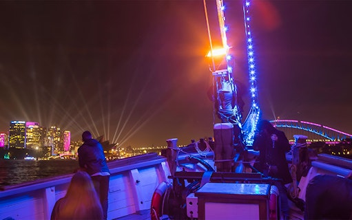Tall ship deck during Vivid Sydney, with illuminated city skyline and Harbour Bridge in view.