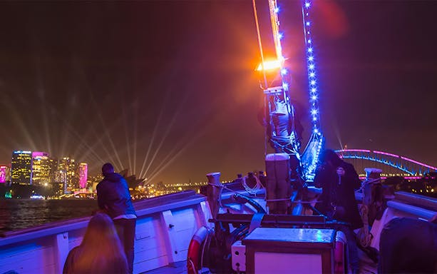 Tall ship deck during Vivid Sydney, with illuminated city skyline and Harbour Bridge in view.